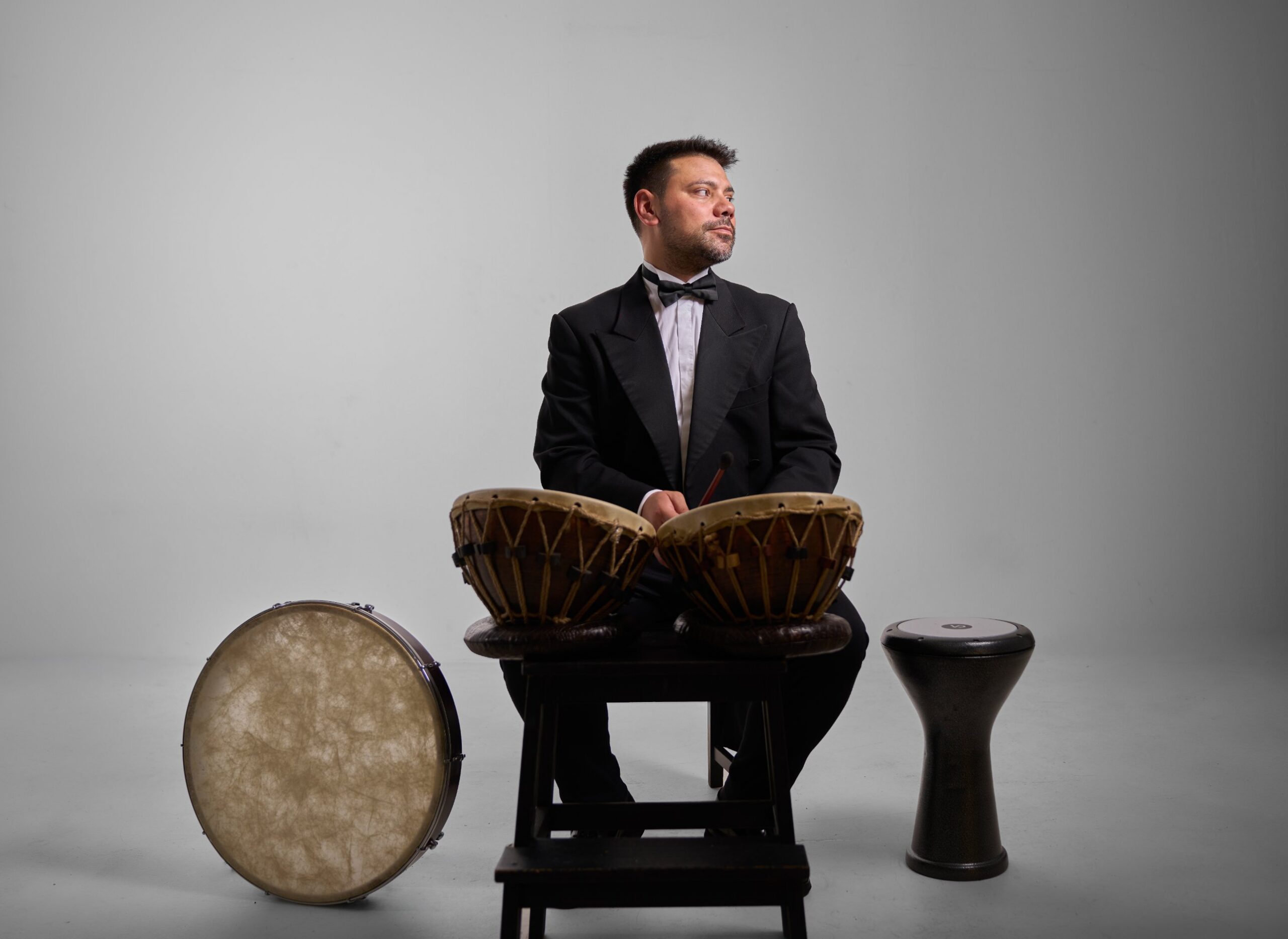 Aykut Köselerli, frak içinde kudümün başında; bir yanında bendir, diğer yanında darbuka